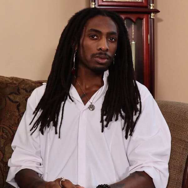 A stylish man with dreadlocks and jewelry, attending the New Living Expo for holistic health and spiritual growth.
